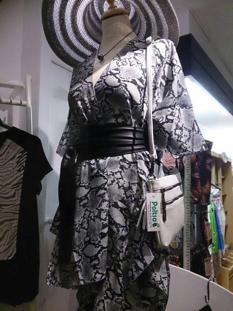 A mannequin dressed in a black and white snakeskin print dress with a wide black belt, styled with a large black-and-white striped sun hat and a white shoulder bag with a visible Poltsa tag.